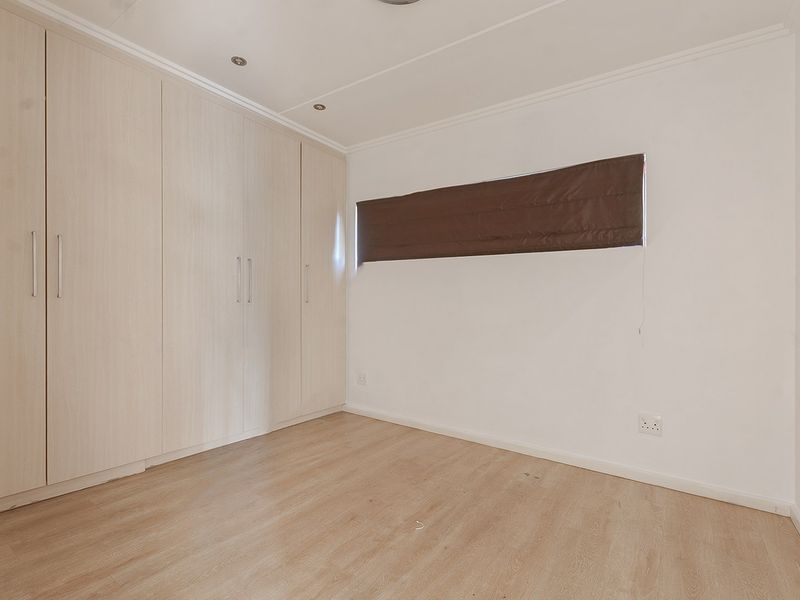 A clean, empty bedroom featuring light wood-tone laminate flooring, ample built-in cupboard storage, and recessed ceiling lighting.