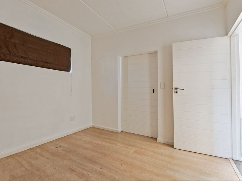 A bright, empty bedroom featuring light-toned laminate flooring, clean white walls, and internal doors, providing a versatile space ready for personalization.