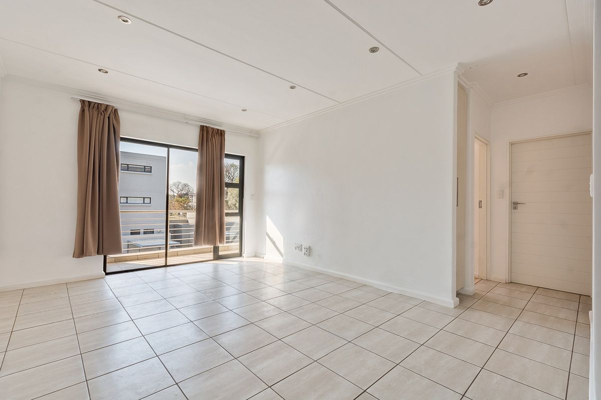 A bright, empty living room featuring neutral tiled flooring, recessed lighting, and a sliding glass door leading to a balcony.