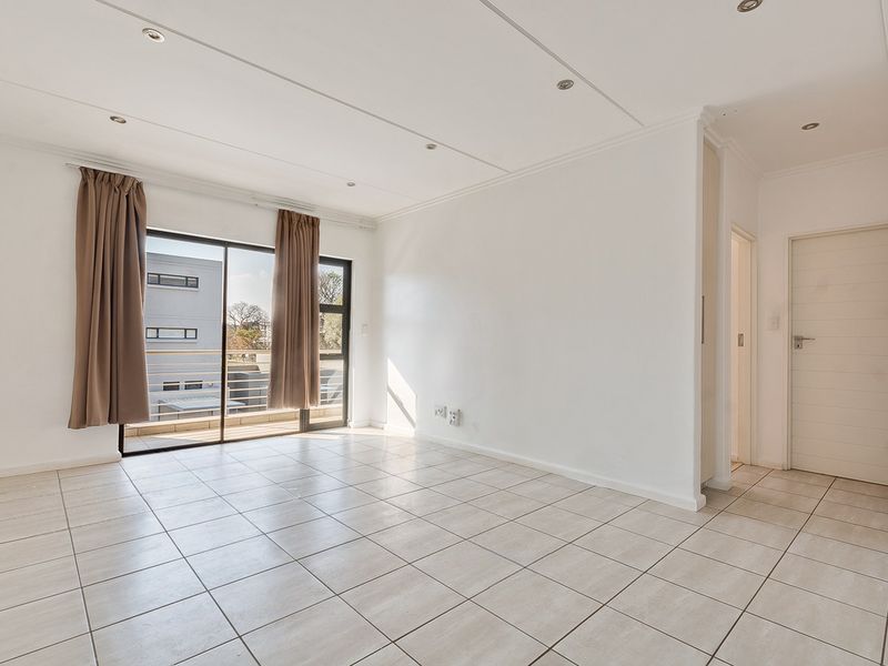 A bright, empty living room featuring neutral tiled flooring, recessed lighting, and a sliding glass door leading to a balcony.