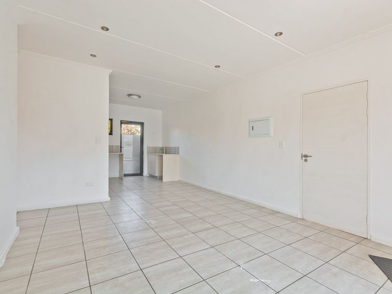A bright, open-plan living area featuring neutral tiled flooring, recessed lighting, and a compact kitchenette area with direct access to the exterior.