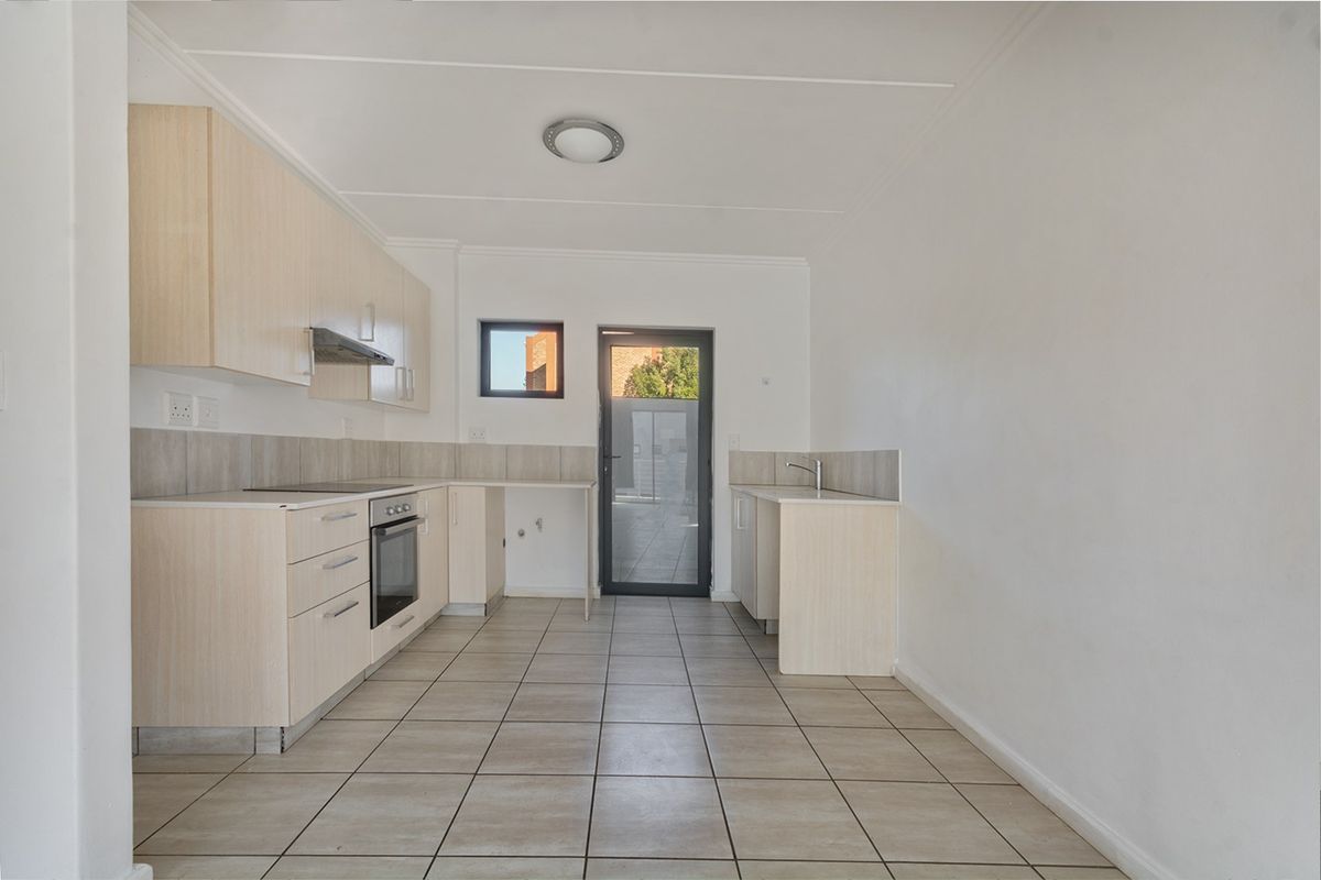 A clean, empty kitchen featuring light wood-finish cabinetry, tiled flooring, built-in oven with extractor fan, and direct access to an outdoor area.