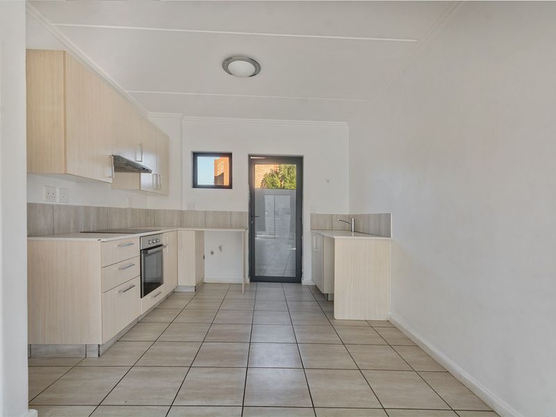 A clean, empty kitchen featuring light wood-finish cabinetry, tiled flooring, built-in oven with extractor fan, and direct access to an outdoor area.