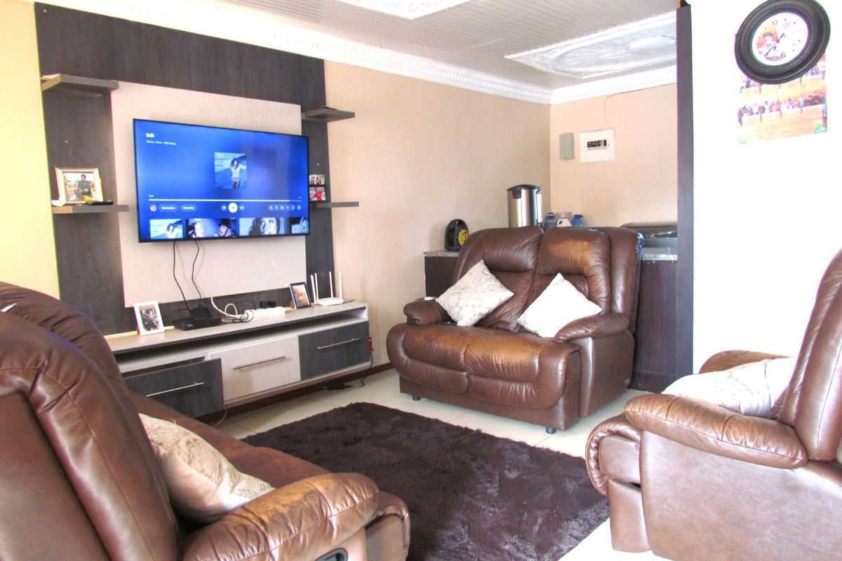 A living room featuring tiled flooring, decorative ceiling cornices, and a built-in media wall unit.
