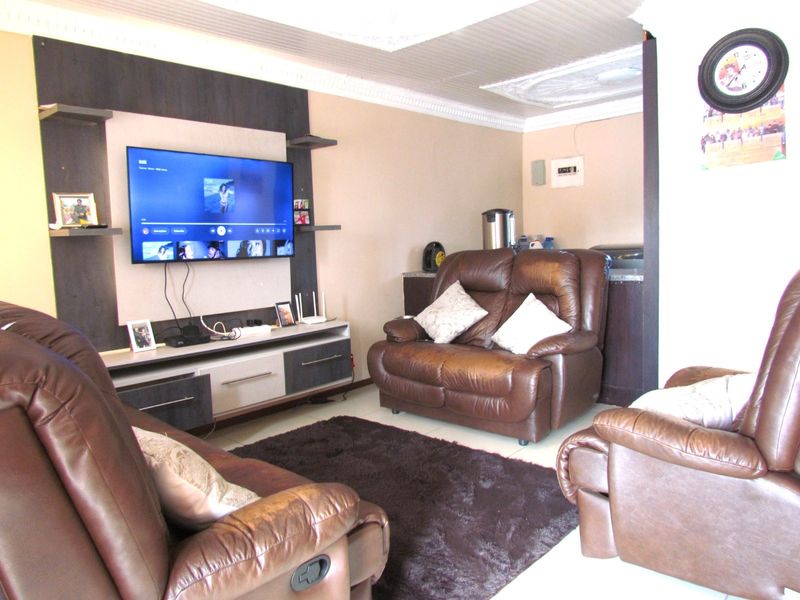 A living room featuring tiled flooring, decorative ceiling cornices, and a built-in media wall unit.