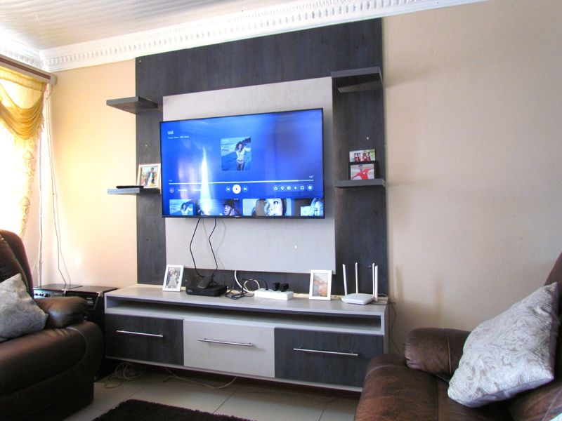 A living room featuring a modern built-in media unit with integrated shelving and tiled flooring, accented by decorative ceiling cornicing.