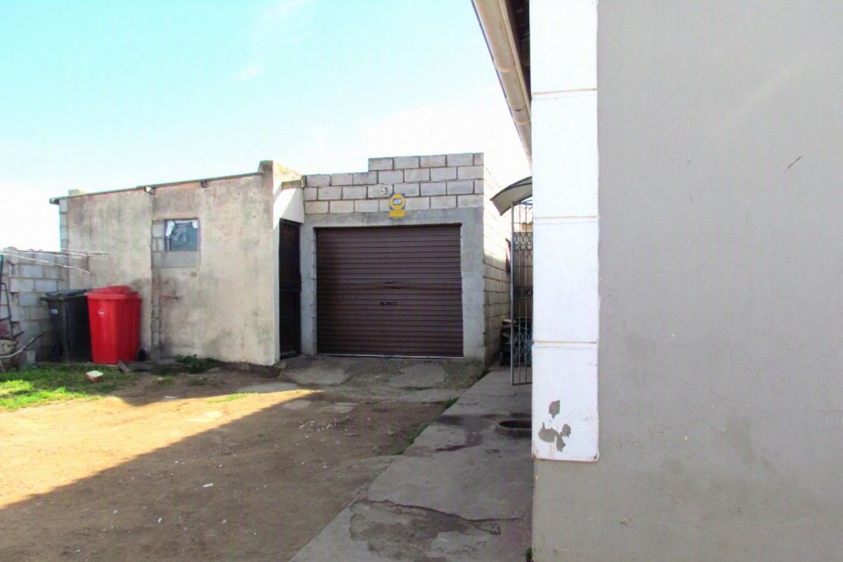 Rear exterior view showing a detached garage with a roller shutter door, concrete block construction, and paved driveway area.