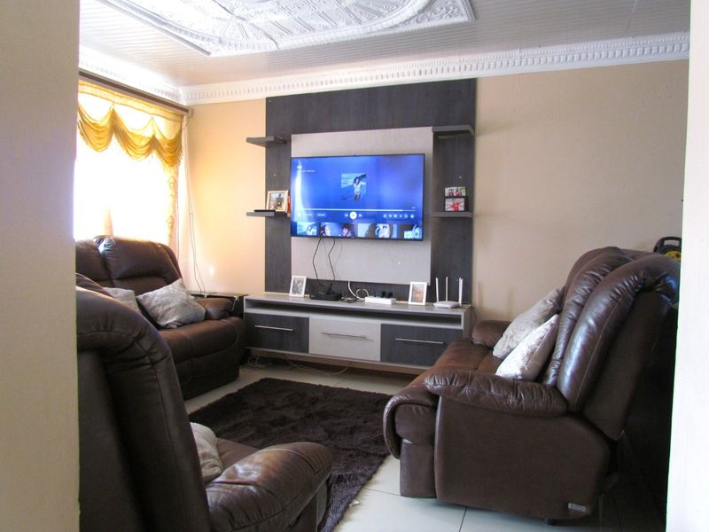 A comfortable living room featuring a built-in media unit, decorative ceiling molding, and tiled flooring, providing a functional space for relaxation.