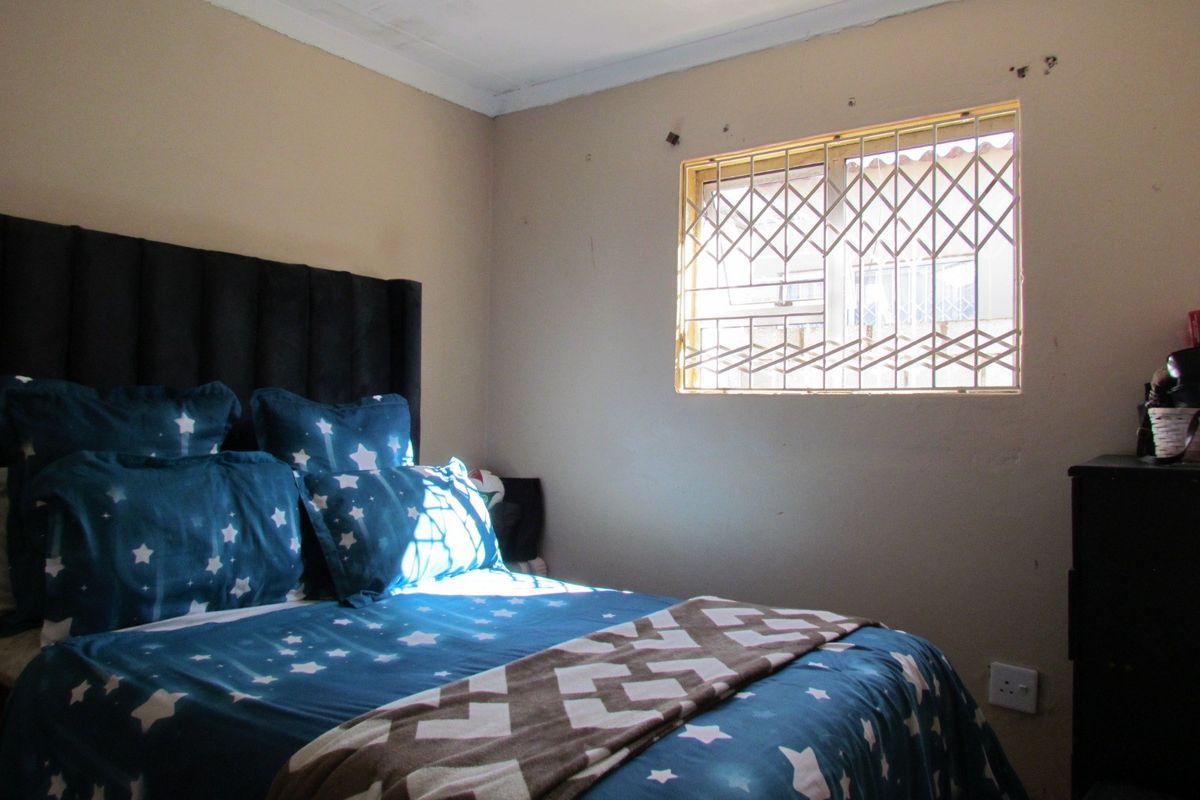 A bedroom featuring a window with a security gate and standard electrical fixtures, requiring minor cosmetic updates to the wall finishes.