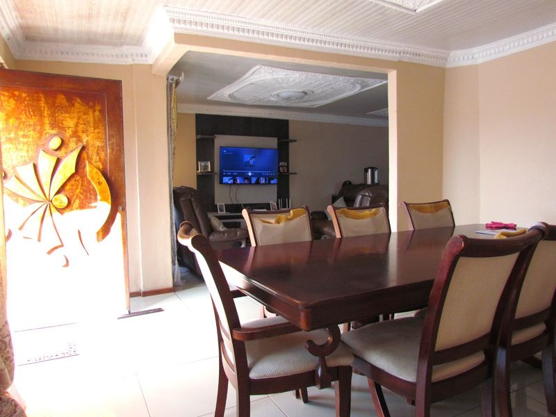 Open plan dining and living area featuring decorative ceiling detailing, tiled flooring, and a built-in media wall unit.