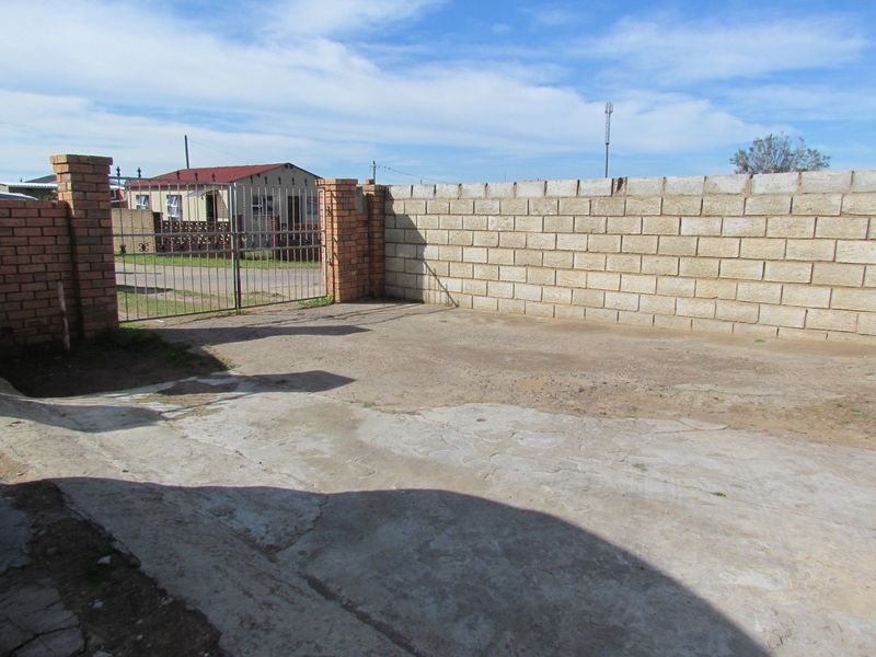 Front exterior area featuring a concrete driveway, metal gate, and brick boundary walling.