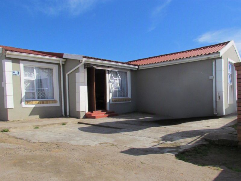 Front elevation of a single-story house featuring a concrete driveway, corrugated metal roof, and aluminium window frames.