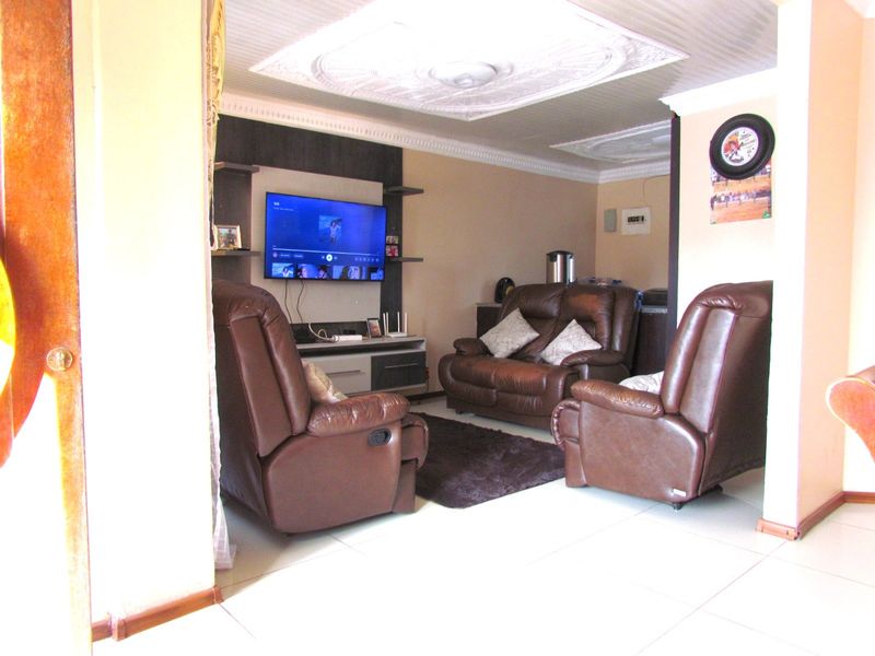 A comfortable living room featuring tiled flooring, decorative ceiling detailing, and a built-in media unit for entertainment.