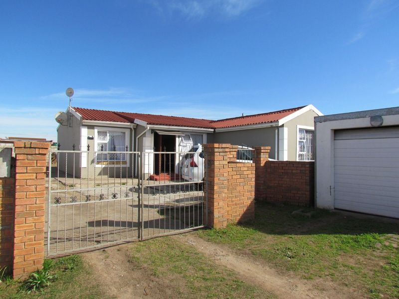 Front view of a single-story house featuring a tiled roof, brick boundary wall with metal gate, and an attached garage.