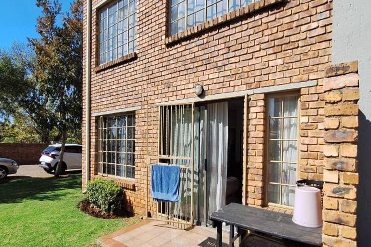Rear view of the apartment featuring a face brick facade, sliding door access with security gate, and a small tiled patio area.