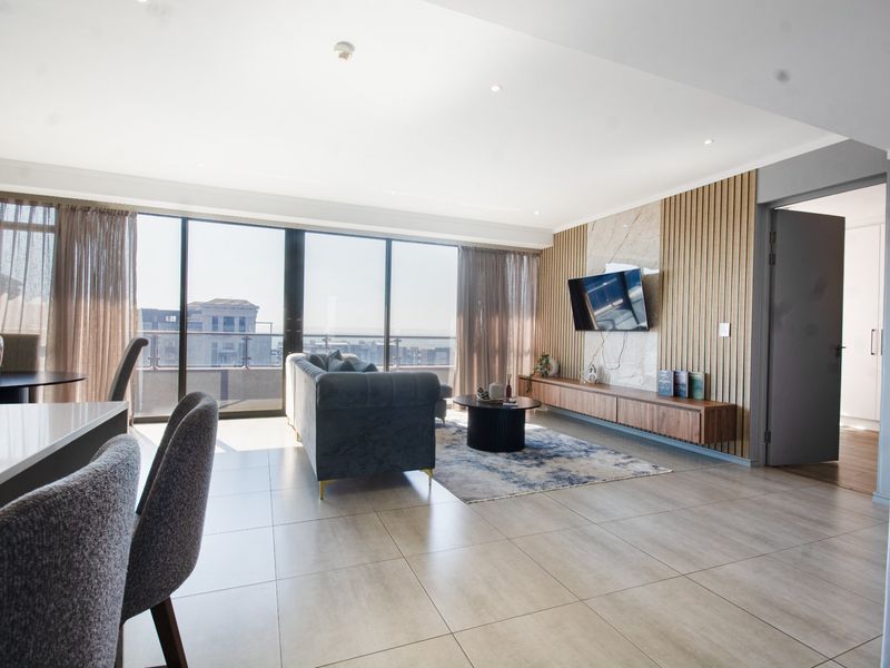 Modern open-plan living area featuring large floor-to-ceiling windows, sleek tiled flooring, and a sophisticated media wall with timber slats and marble accents.