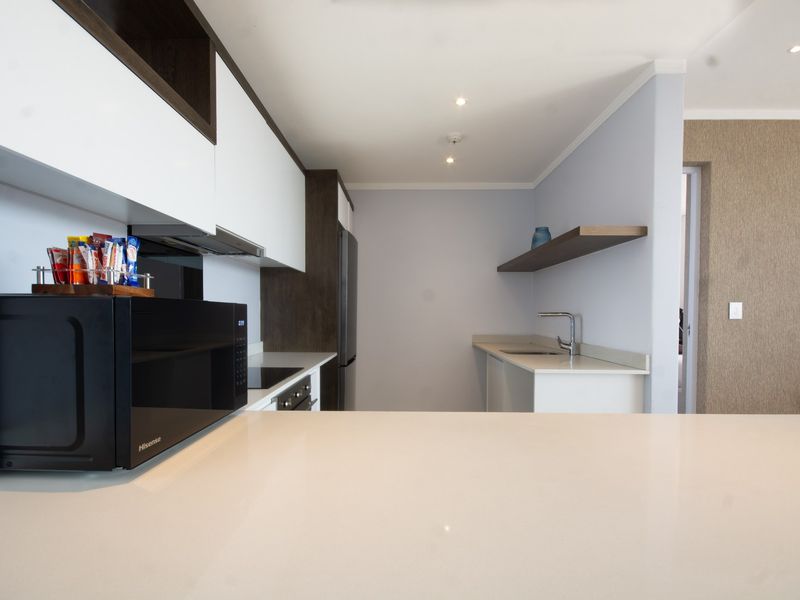 Modern kitchen featuring sleek white and dark wood cabinetry, quartz countertops, integrated appliances, and minimalist floating shelving.
