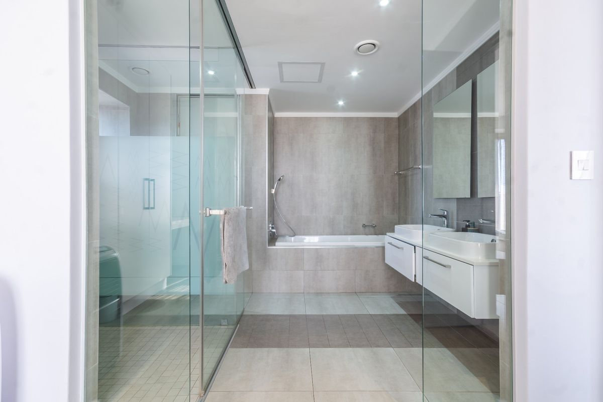 Modern bathroom featuring a glass-enclosed shower, built-in bathtub, and a sleek wall-mounted double vanity with contemporary tiling throughout.