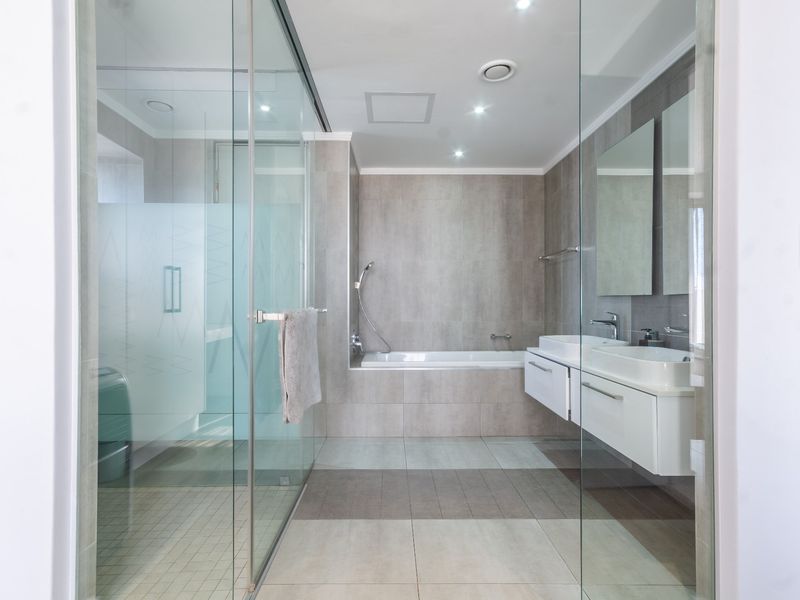 Modern bathroom featuring a glass-enclosed shower, built-in bathtub, and a sleek wall-mounted double vanity with contemporary tiling throughout.