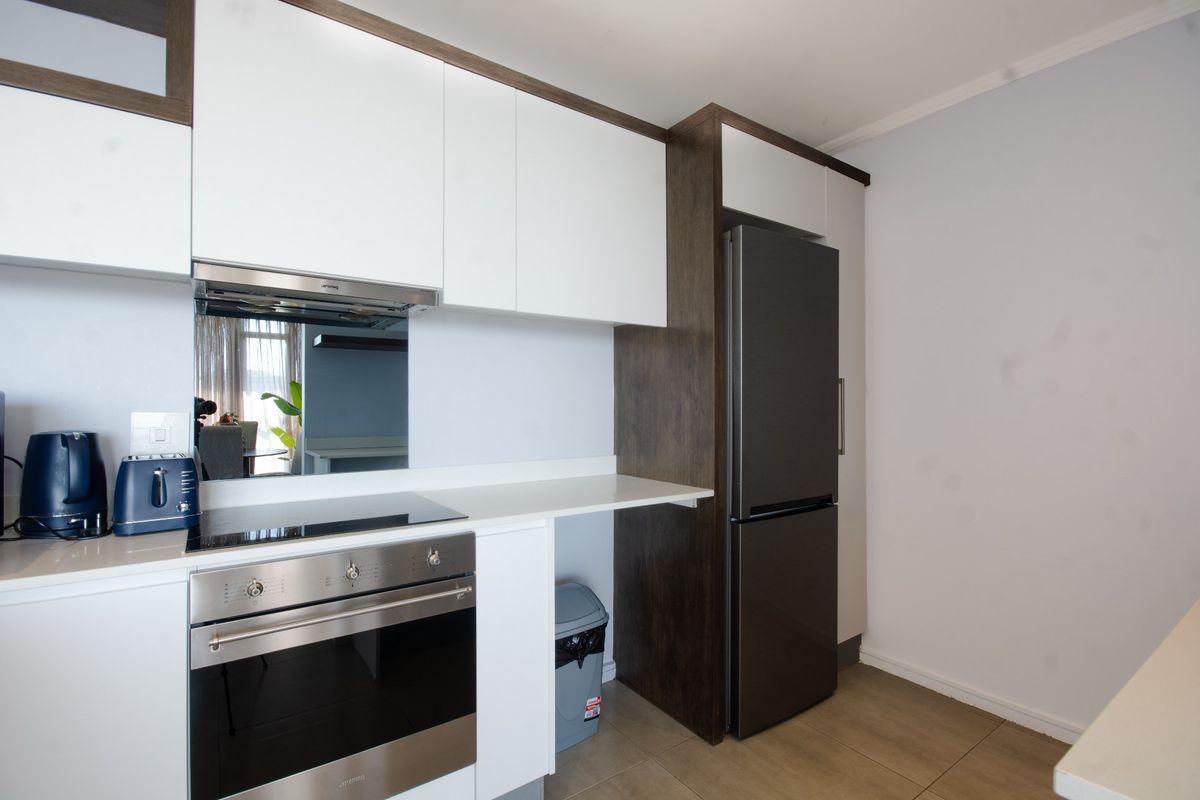 Modern kitchen featuring sleek white cabinetry, dark wood accents, stone countertops, and integrated stainless steel appliances including an oven and hob.