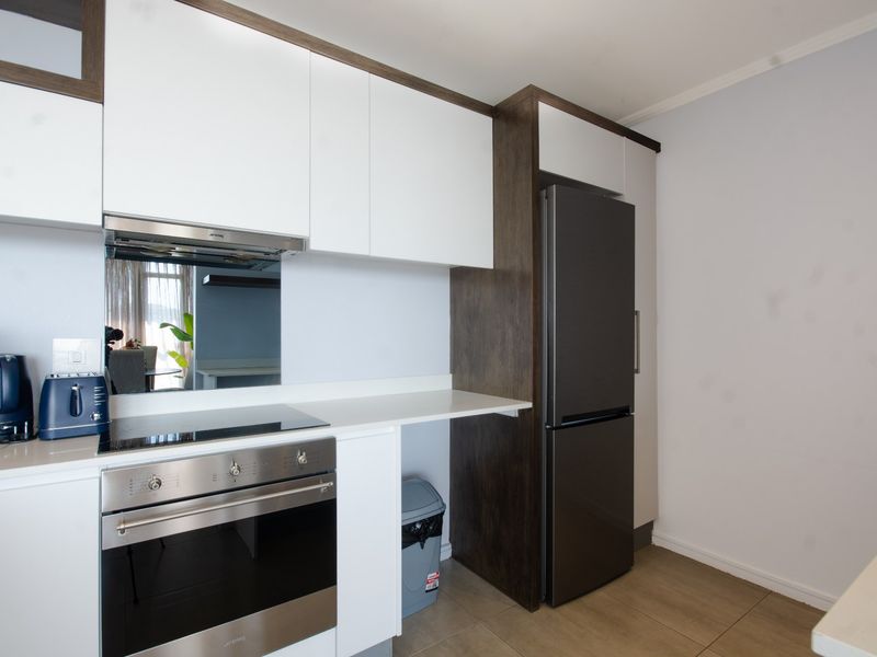 Modern kitchen featuring sleek white cabinetry, dark wood accents, stone countertops, and integrated stainless steel appliances including an oven and hob.