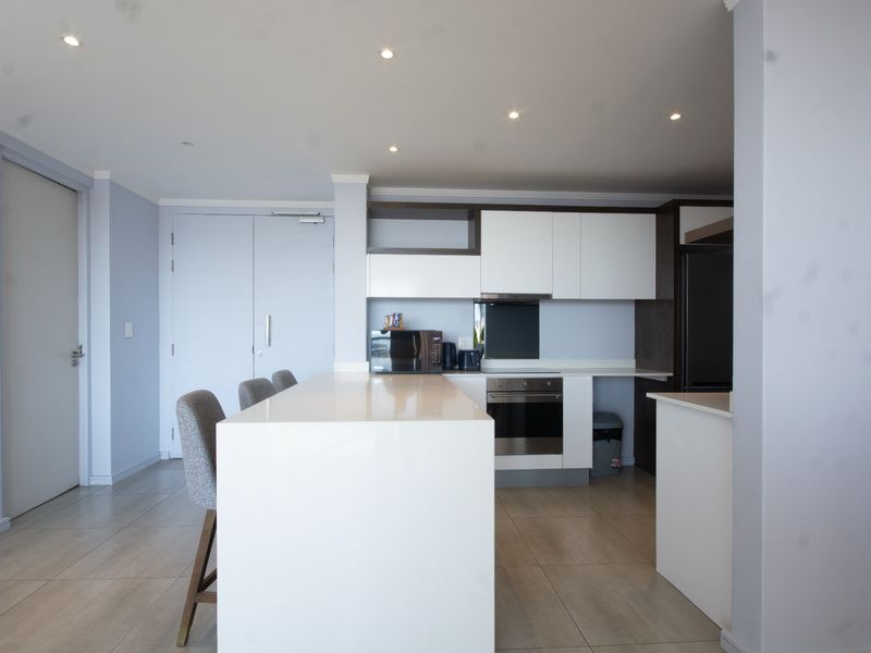 Modern open-plan kitchen featuring a central island with quartz countertops, built-in oven, extractor fan, and sleek cabinetry, complemented by neutral tiled flooring.