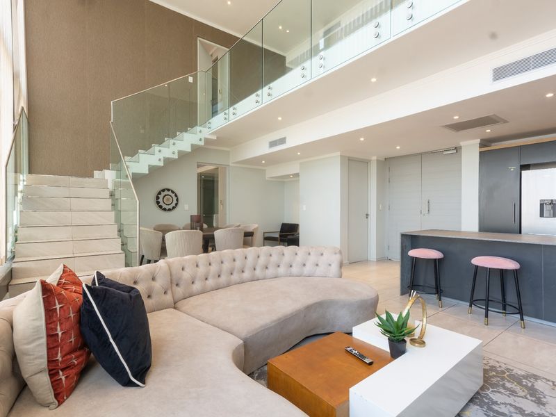 Spacious open-plan living area featuring a modern glass-railed staircase, contemporary kitchen island, and high-end finishes throughout this sophisticated apartment interior.