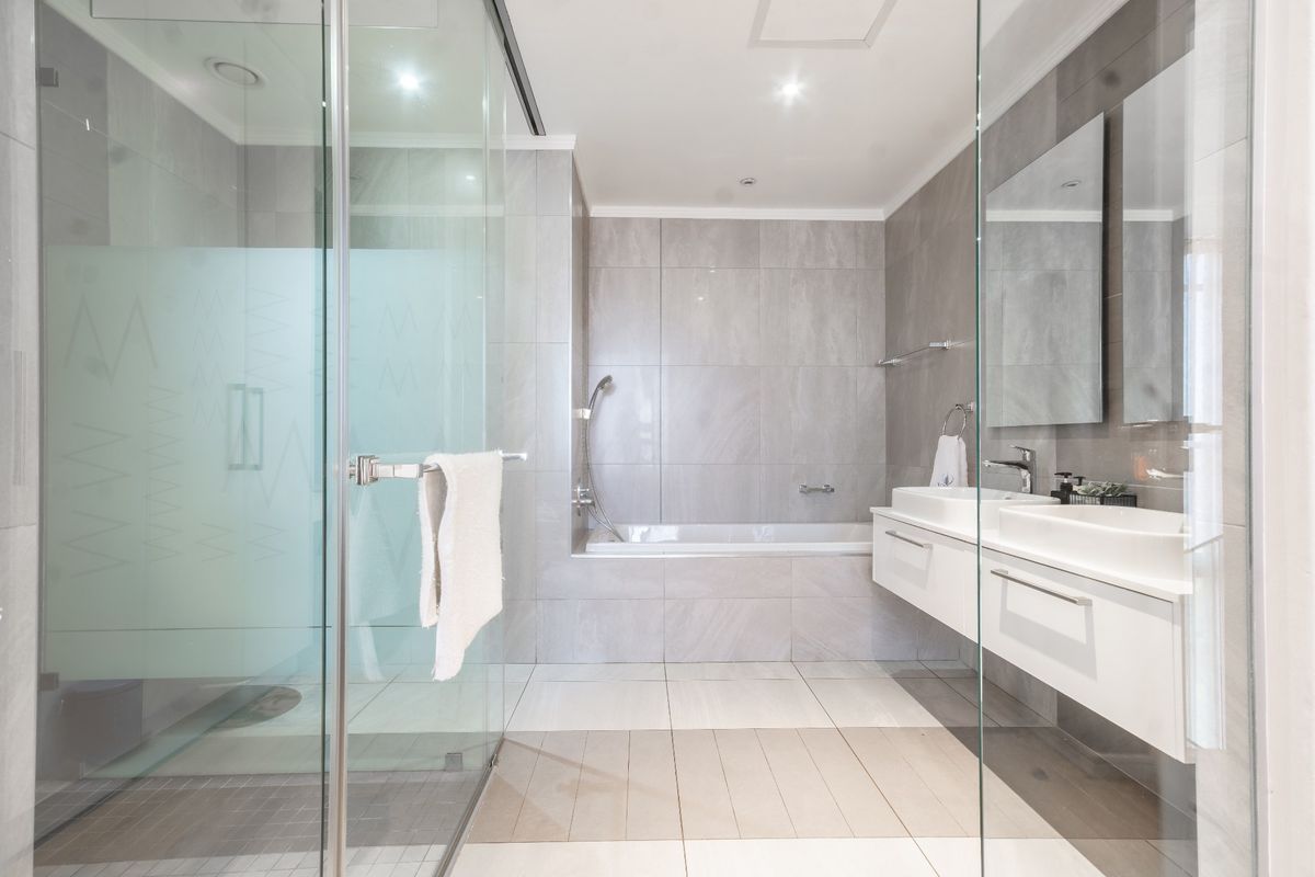 Modern bathroom featuring a glass-enclosed shower, built-in bathtub, and a sleek wall-mounted double vanity with integrated sinks and neutral tiling.