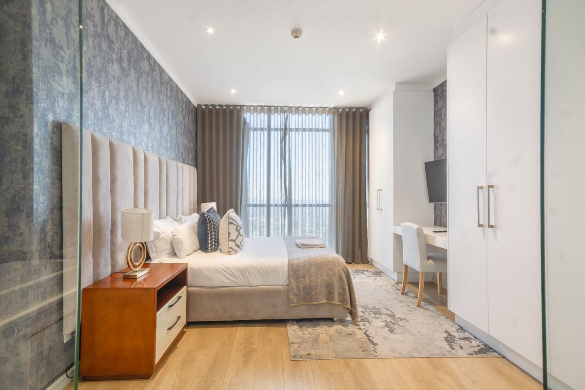 Modern bedroom featuring laminate flooring, built-in wardrobes, a integrated desk, and recessed downlighting, offering a clean and functional living space.