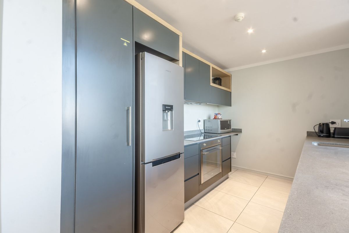 Modern kitchen featuring dark grey cabinetry, stone countertops, integrated oven, electric hob, and tiled flooring in a clean, contemporary layout.
