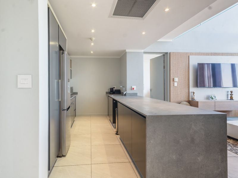 Modern open-plan kitchen featuring a sleek stone island, integrated cabinetry, and recessed lighting, seamlessly flowing into the adjacent living area.