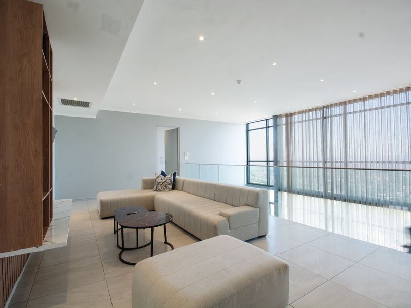 Modern open-plan living area featuring large floor-to-ceiling windows, sleek tiled flooring, recessed lighting, and a custom built-in shelving unit.