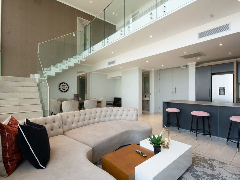 Modern open-plan living area featuring a striking glass staircase, contemporary kitchen with island, and high-end finishes throughout this spacious apartment interior.