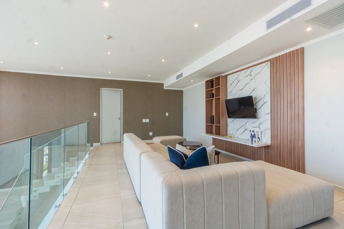 Modern living area featuring a sleek built-in media unit with marble and timber accents, glass balustrade, and recessed ceiling lighting.