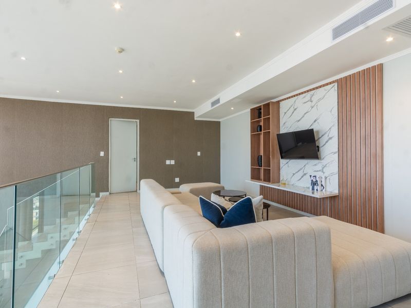 Modern living area featuring a sleek built-in media unit with marble and timber accents, glass balustrade, and recessed ceiling lighting.