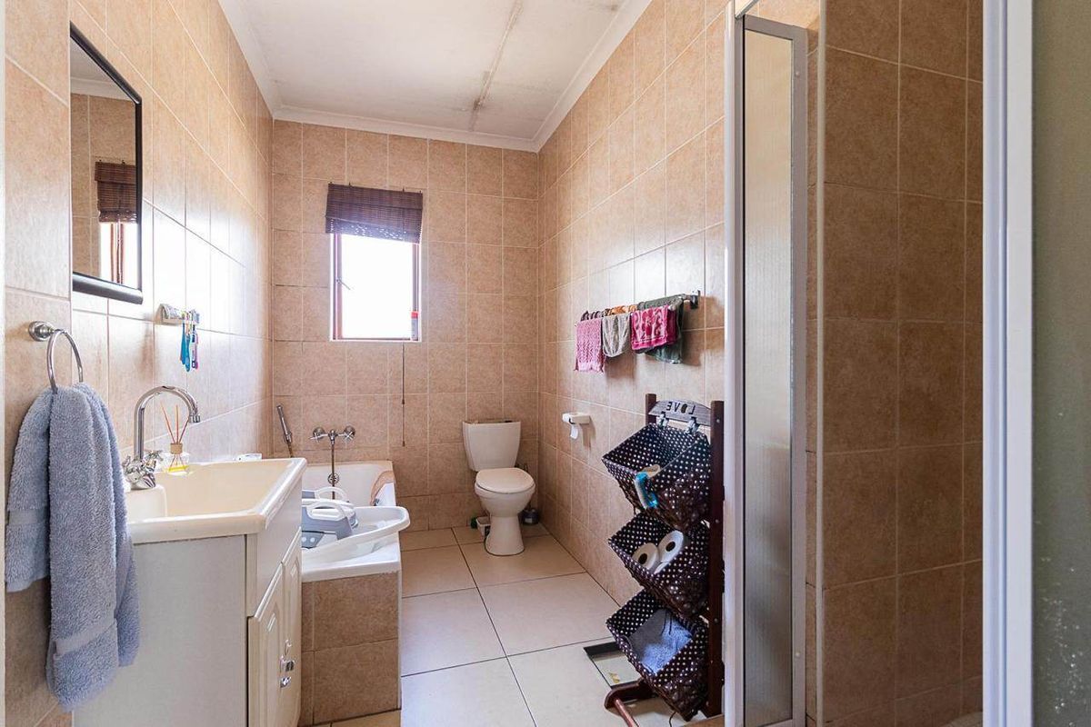 A dated bathroom featuring a vanity basin, built-in bathtub, toilet, and shower enclosure with full-height wall tiling and visible ceiling water damage.