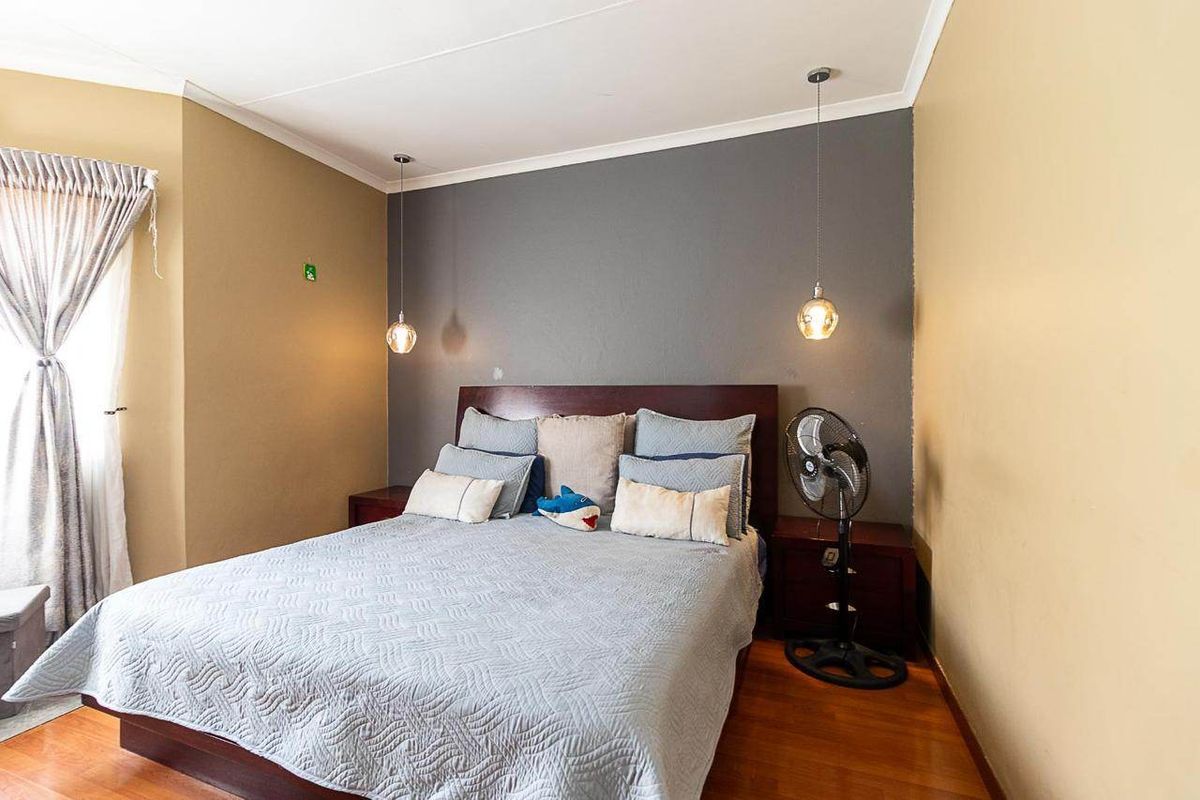 A bedroom featuring hardwood flooring, a dark accent wall, and modern pendant lighting fixtures.
