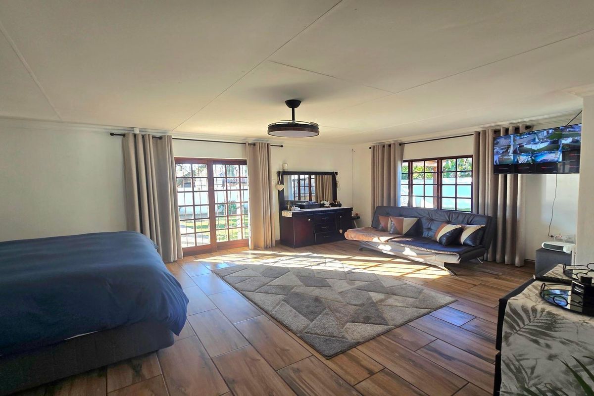 Spacious bedroom featuring timber-look floor tiles, large windows, and direct access to the exterior through classic french doors.