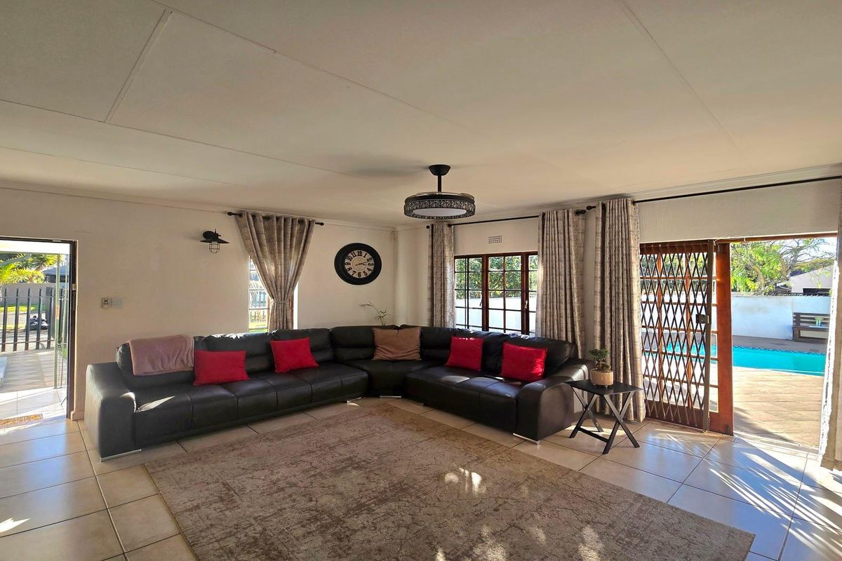 Spacious living room featuring tiled flooring, large windows, and direct access to the outdoor pool area through a security-fitted sliding door.