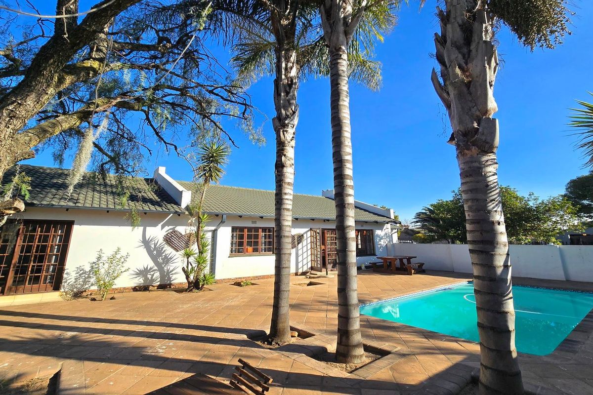 Rear exterior view featuring a swimming pool, paved patio area, and established palm trees set against the back facade of the house.