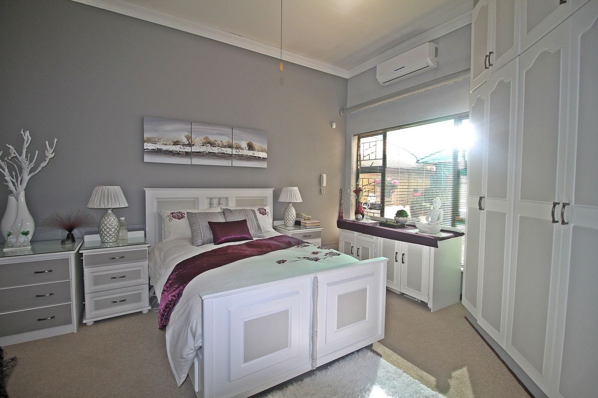A well-maintained bedroom featuring built-in cupboards, a split-system air conditioner, and large windows with security burglar bars.