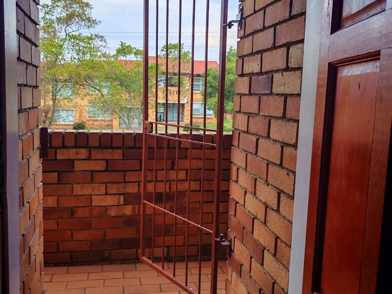 A private balcony featuring exposed brick walls, tiled flooring, and a secure metal gate, offering an outdoor space accessible through an arched doorway.
