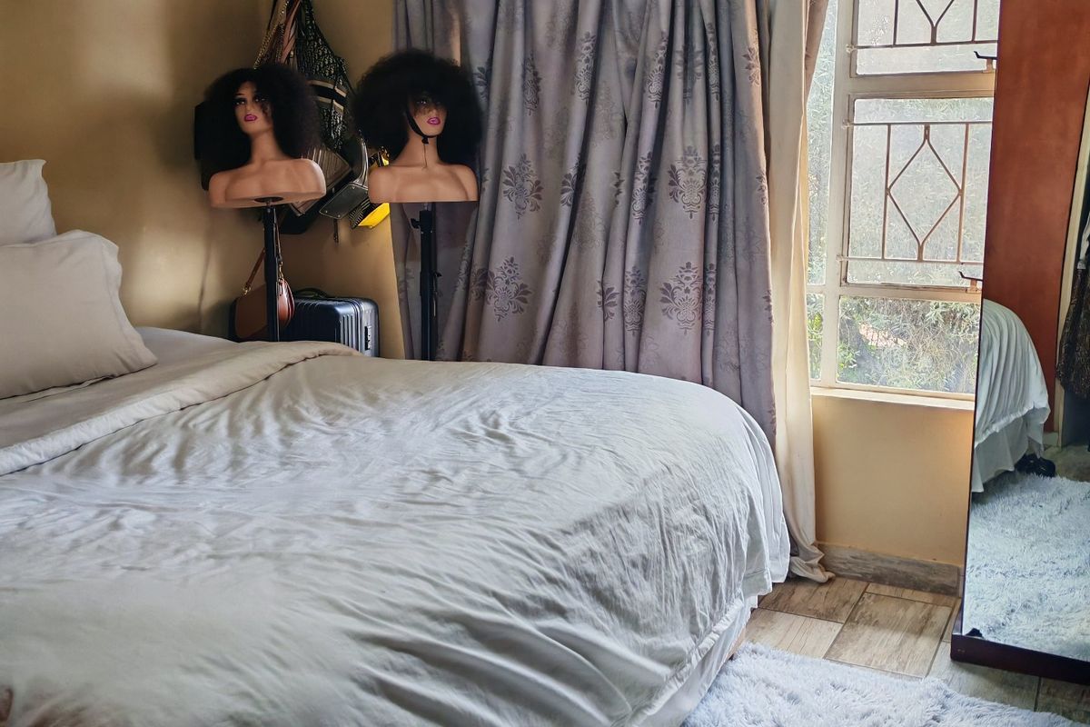 A bedroom featuring tiled flooring and a window fitted with security bars, providing natural light through the curtained window.