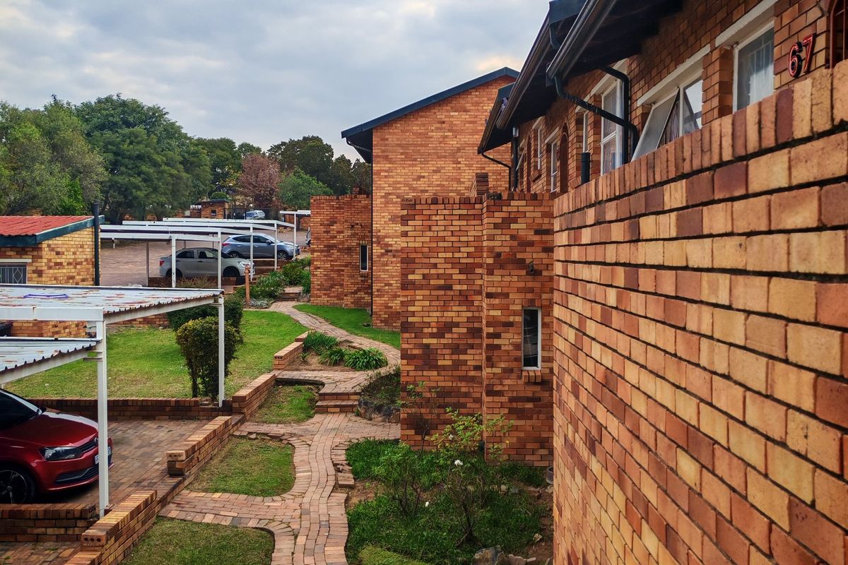 Exterior view of a face brick apartment complex featuring paved walkways, landscaped garden areas, and covered parking bays.