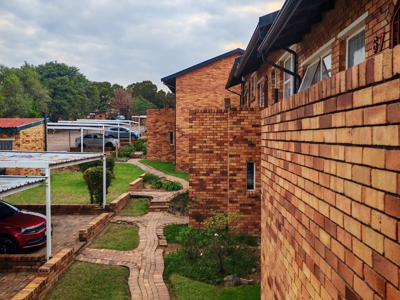 Exterior view of a face brick apartment complex featuring paved walkways, landscaped garden areas, and covered parking bays.