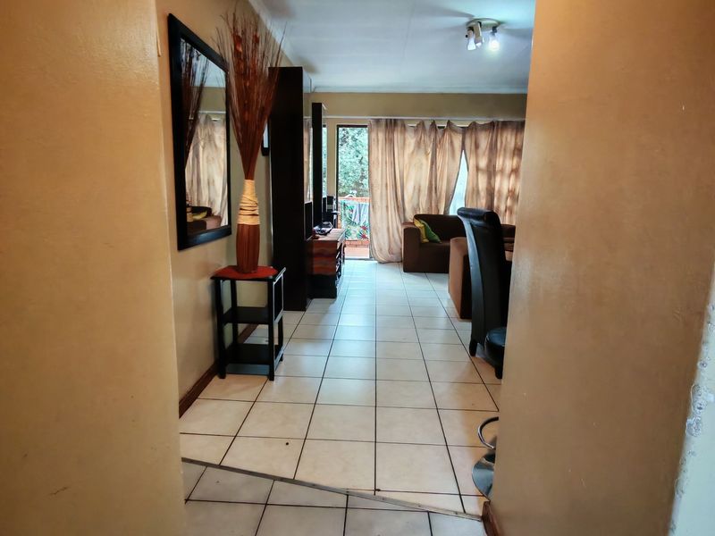 A view from the hallway into an open-plan living area featuring ceramic tiled flooring and access to an outdoor balcony through a sliding glass door.