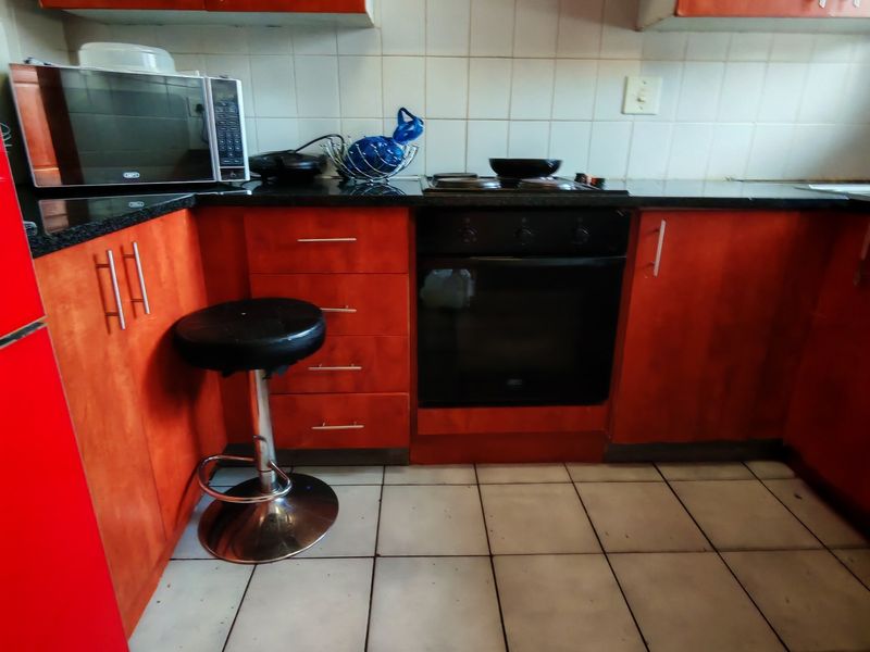 Compact kitchen featuring wooden cabinetry, granite countertops, tiled backsplash, and built-in oven with electric hob.
