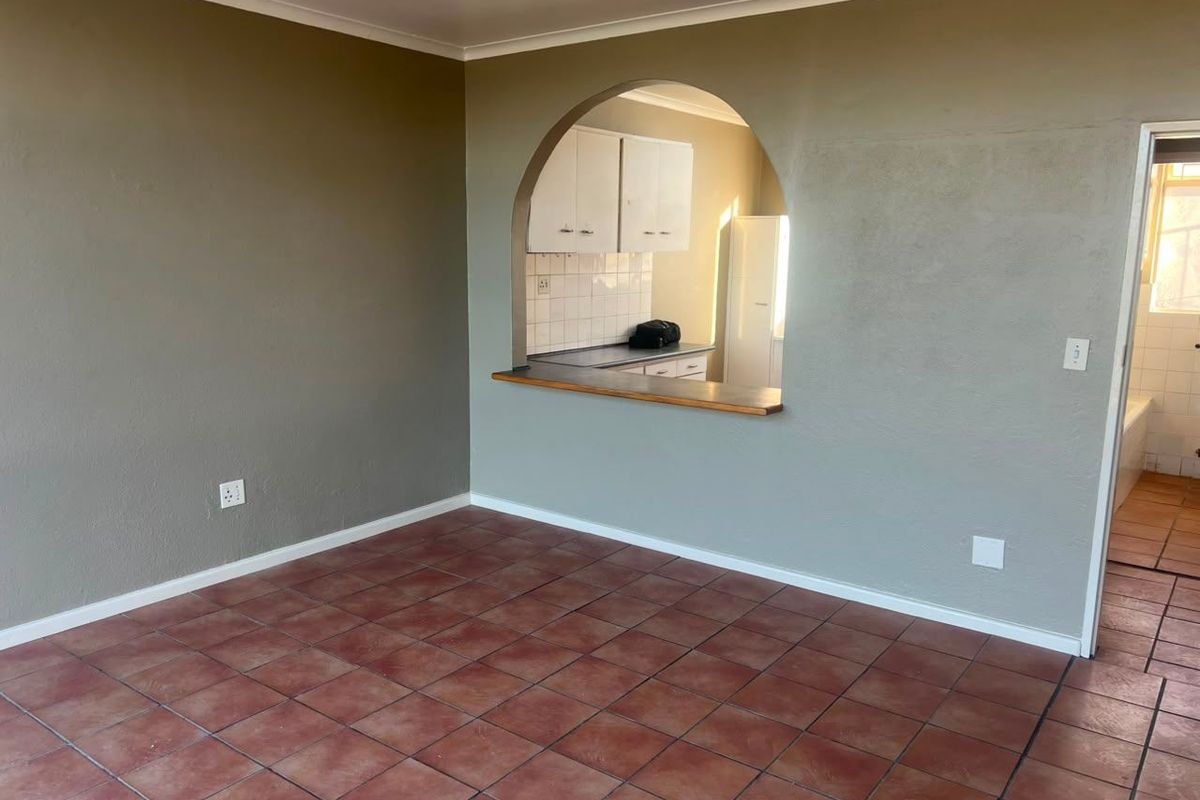 An empty living area featuring terracotta-style floor tiles and an arched opening looking through to the kitchen area.