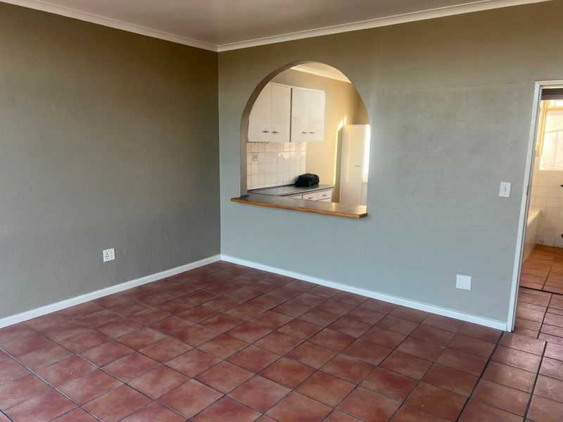 An empty living area featuring terracotta-style floor tiles and an arched opening looking through to the kitchen area.