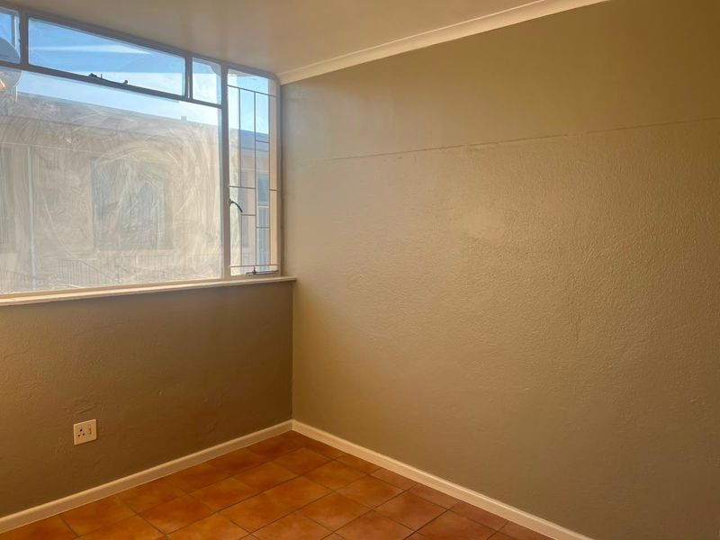 An empty bedroom featuring tiled flooring, a large window with security bars, and neutral painted walls with visible surface imperfections.